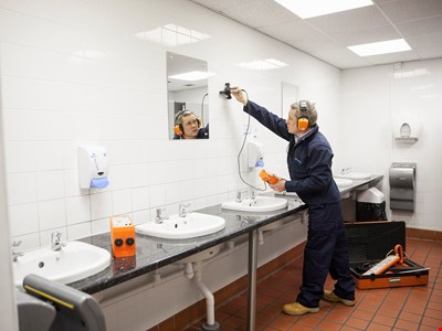 En teknker står i ett badrum med handfat och mäter i väggen.